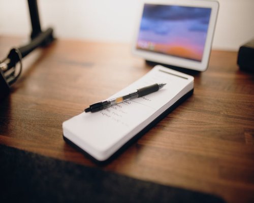 Notepad and pen resting on a desk next to a digital tablet